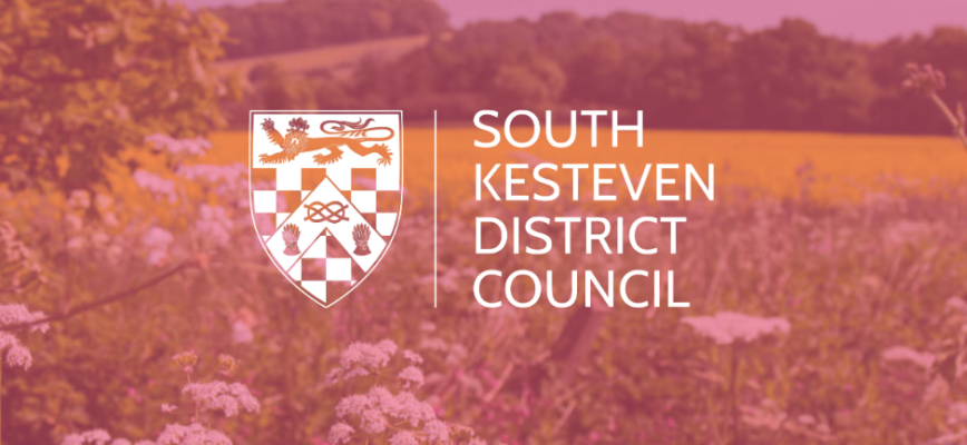 Field landscape in the background. Pink screen overlaid on the screen. South Kesteven District Council logo in the centre.